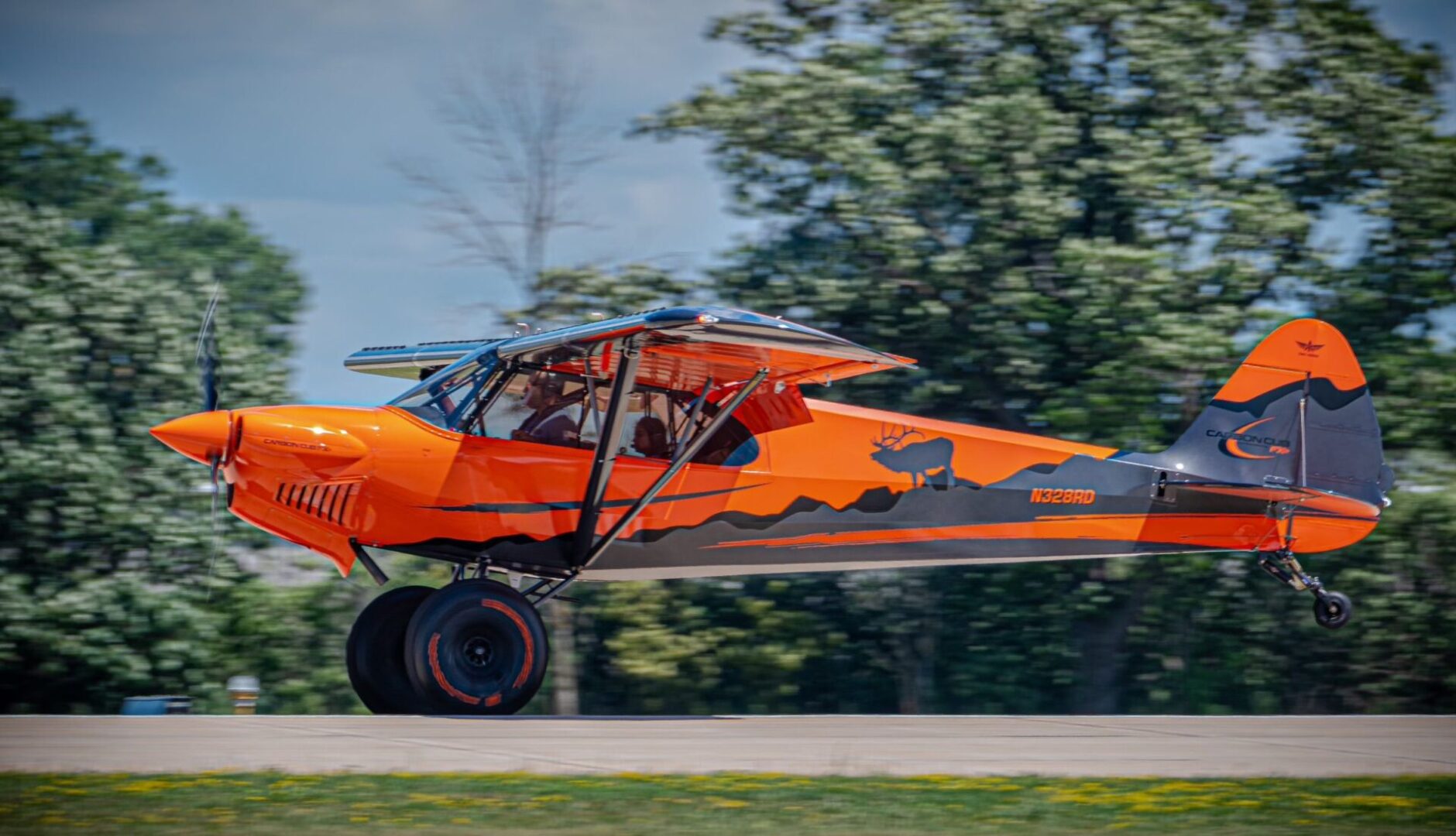 A small orange airplane is flying on the road.
